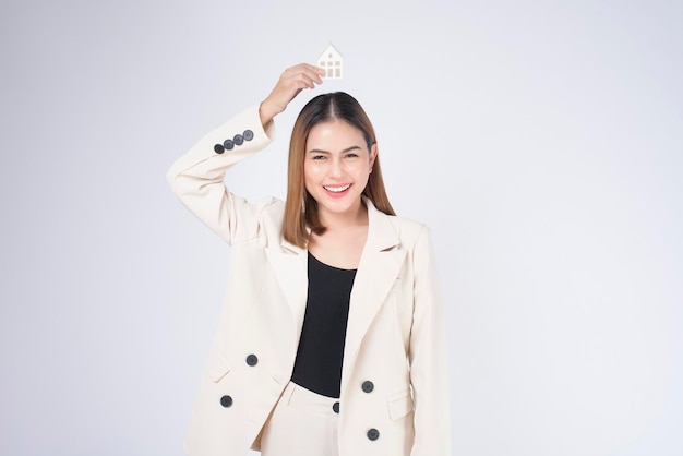 Young beautiful woman in suit holding small model house over white background studio