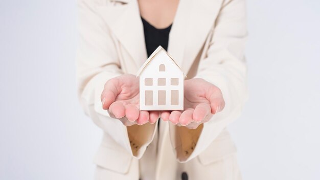 Young beautiful woman in suit holding small model house over white background studio