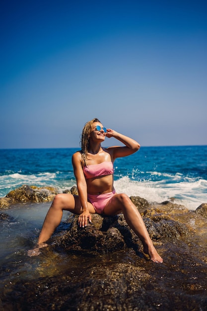 Young beautiful woman in a swimsuit sits on a rocky beach of the Mediterranean sea in Turkey The concept of sea recreation Selective focus