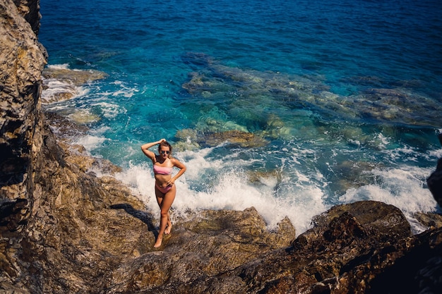 Young beautiful woman in a swimsuit stands on a rocky beach of the Mediterranean Sea The concept of sea recreation Selective focus
