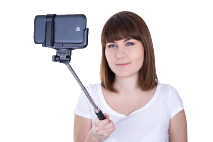 Young beautiful woman taking photo on smart phone with selfie stick isolated on white background