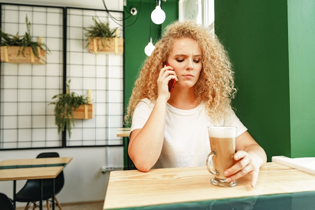 カフェテリアで電話で話している若い美しい女性