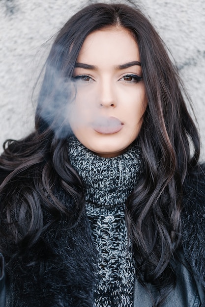 Young beautiful woman tanding in front a wall with cigarette