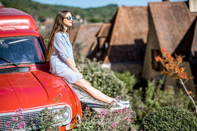 Young beautiful woman traveling by the red retro car in the old french village