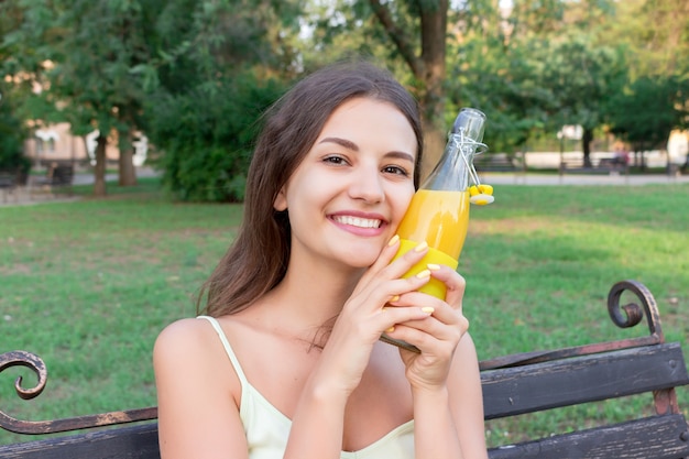 Young beautiful woman tries to refresh with a cold bootle of juice in a hot summer day