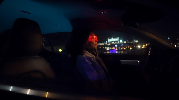 Photo young beautiful woman uses virtual reality glasses in the car during late rainy night with back view