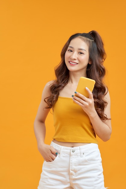黄色の背景に携帯電話スタジオを使用して若い美しい女性