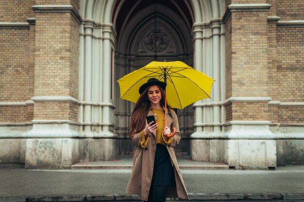 Young beautiful woman using a smartphone and holding a yellow umbrella