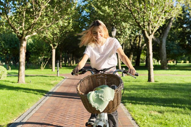 Young beautiful woman on vintage bike with basket rides on nature sunny summer day alley in green park background