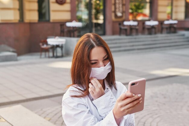 若い美しい女性が街を歩く電話とマスクで通りの女の子の肖像画検疫パンデミック自己隔離covid