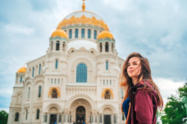 Young beautiful woman walks on the square with the Sea Cathedral in Kronstadt Russia