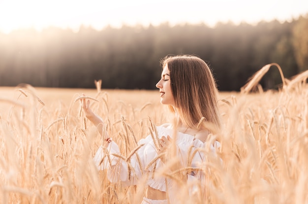 Una giovane bella donna cammina attraverso un campo di grano in abiti bianchi