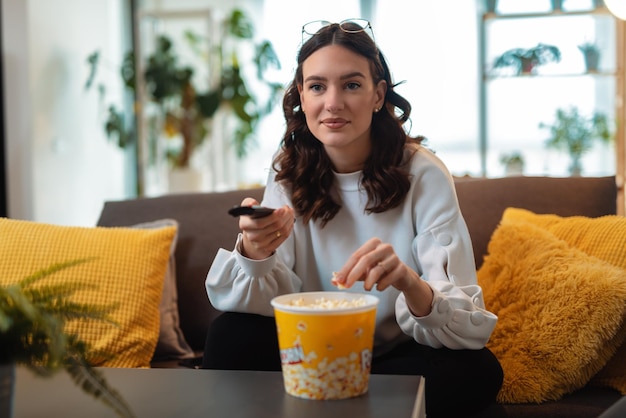 Young beautiful woman watching TV at home and eating pop corn