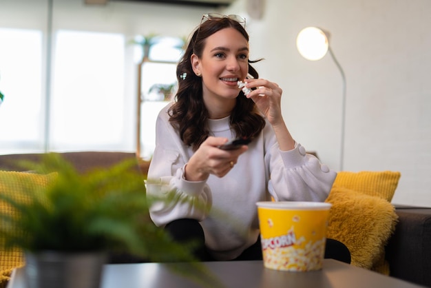 家でテレビを見て、ポップコーンを食べる若い美しい女性