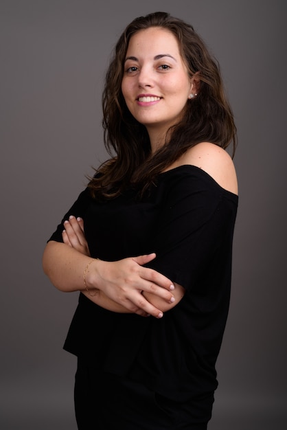 Young beautiful woman wearing black off-shoulder top against gray wall