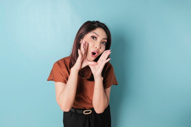 茶色のシャツを着た若い美しい女性が、口のコミュニケーションのコンセプトに手で横に叫び、大声で叫ぶ