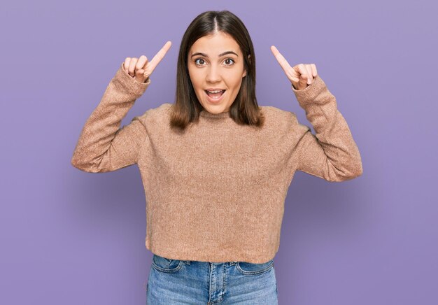 Young beautiful woman wearing casual clothes smiling amazed and surprised and pointing up with fingers and raised arms.