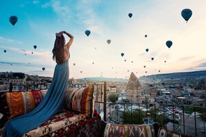 Молодая красивая женщина нося элегантное длинное платье перед ландшафтом cappadocia на солнечности с воздушными шарами в воздухе. турция.