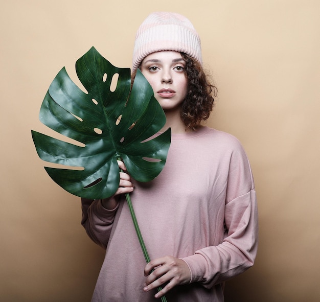 Young beautiful woman wearing pink casual clothes holding leaf of monstera posing on white background