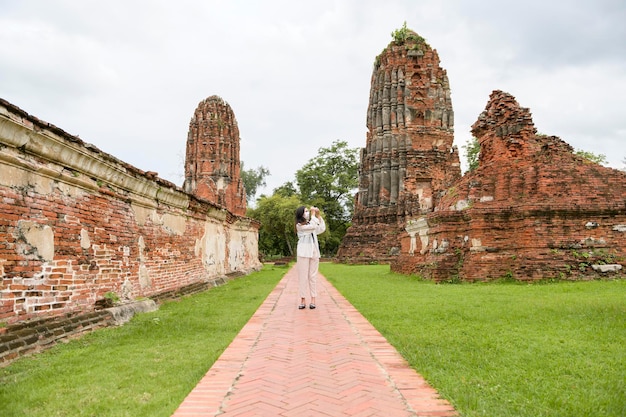 Young beautiful woman wearing protective mask traveling and taking photo at Thai historical Park