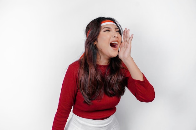 Foto giovane bella donna che indossa un top rosso gridando e urlando forte con una mano sulla bocca concetto di giorno dell'indipendenza dell'indonesia
