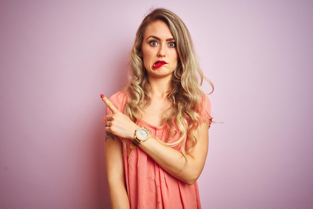 Young beautiful woman wearing tshirt standing over pink isolated background Pointing aside worried and nervous with forefinger concerned and surprised expression