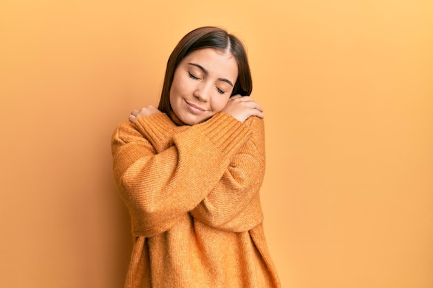 Young beautiful woman wearing turtleneck sweater hugging oneself happy and positive smiling confident self love and self care