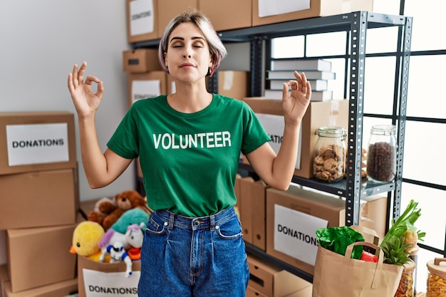 Foto la giovane bella donna che indossa la maglietta volontaria allo stand delle donazioni si rilassa e sorride con gli occhi chiusi facendo il gesto di meditazione con il concetto di yoga delle dita