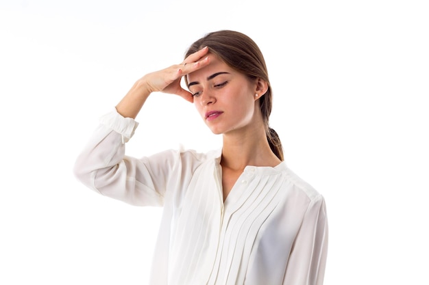 Young beautiful woman in white blouse holding hand at her forehead on white background in studio