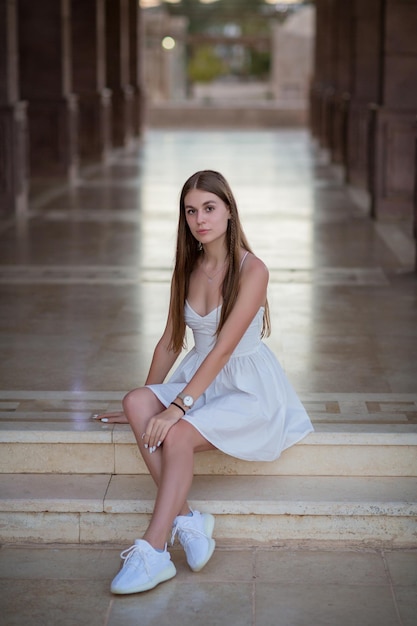 A young beautiful woman in white dress sits on a marble staircase next to a temple in Egypt