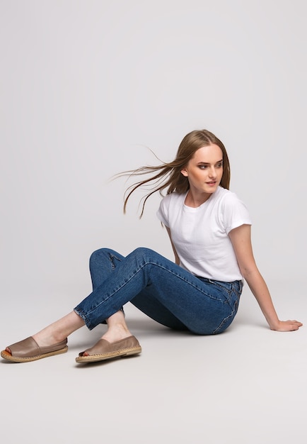 Young beautiful woman in a white t-shirt and jeans on a white floor.