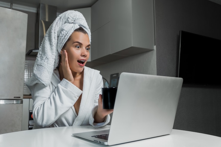 Photo young beautiful woman in white towel and robe drinking coffee and looking on laptop screen at the table