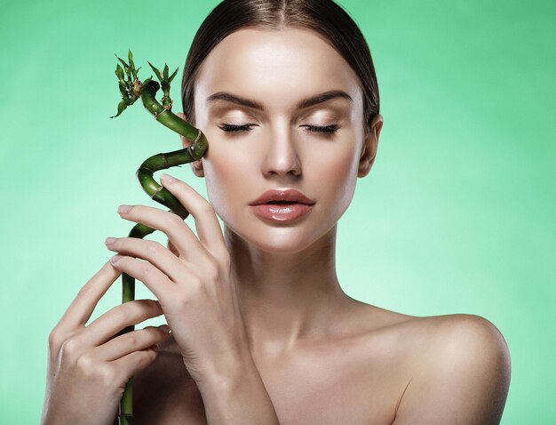 Young beautiful woman with bamboo over green background