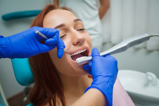 Giovane bella donna con i bei denti bianchi che si siedono su una sedia dentaria.