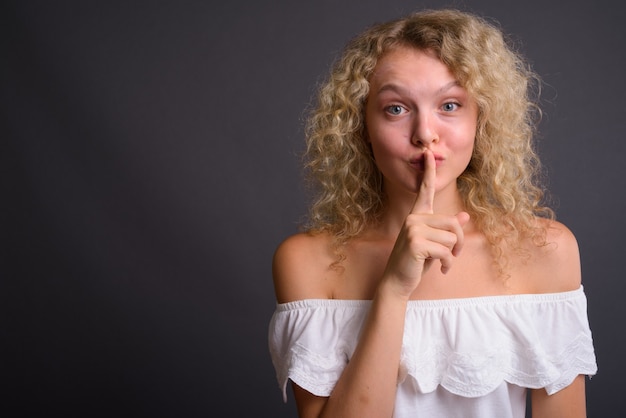 Young beautiful woman with blond curly hair against gray