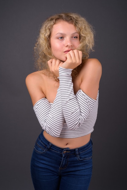 Young beautiful woman with blond curly hair against gray