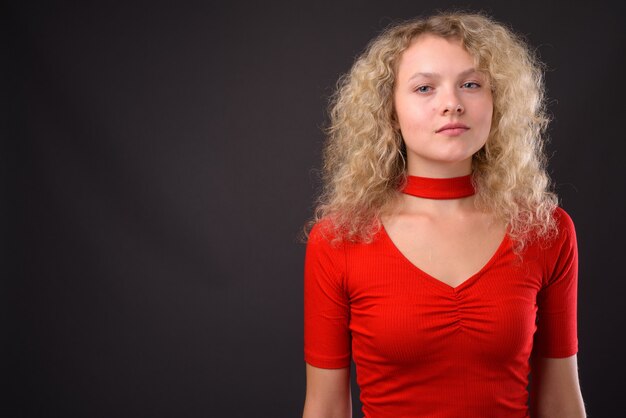 Photo young beautiful woman with blond curly hair against gray