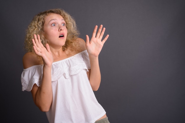 Young beautiful woman with blond curly hair against gray