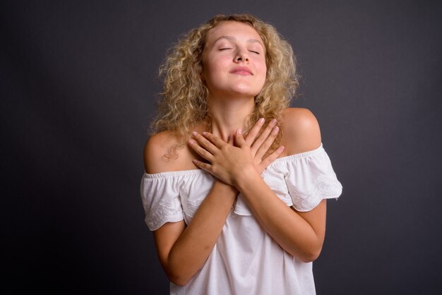 Young beautiful woman with blond curly hair against gray