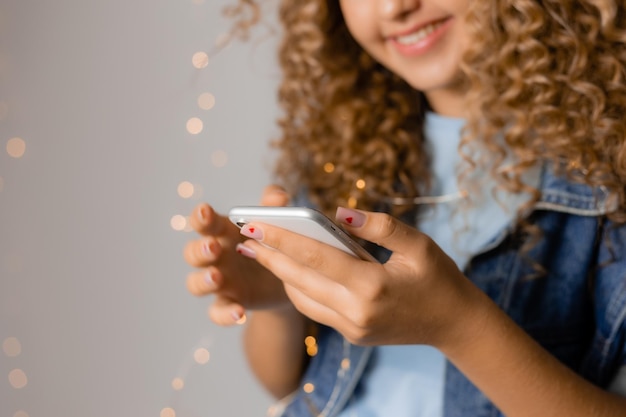 Young beautiful woman with blonde curly hair in a denim jacket is holding a smartphone in her hands. girl communicates online on social networks. blogger. space for text. High quality photo