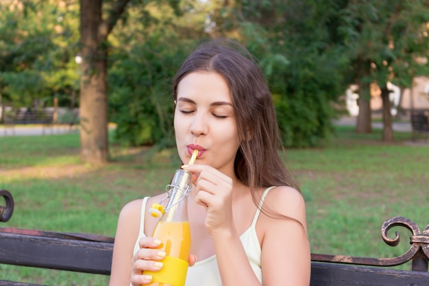 Молодая красивая женщина с бутылкой свежего апельсинового сока наслаждается отличной погодой в парке