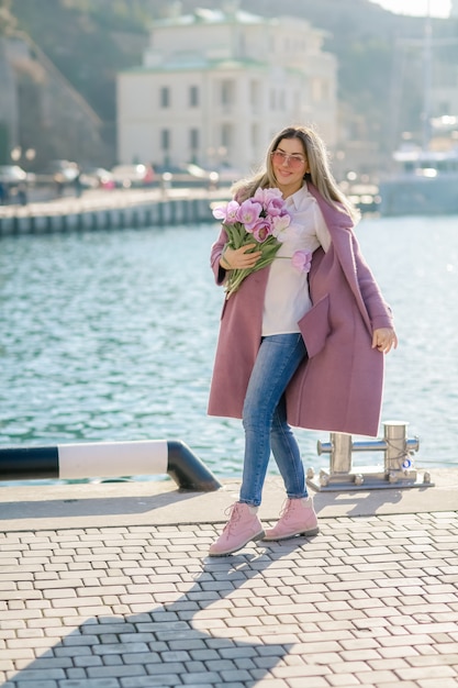 海の海岸に花の花束を持つ若くて美しい女性