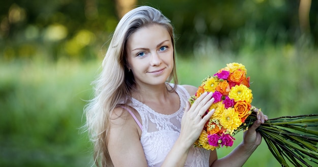 Young beautiful woman with a bright bouquet of flowers, outdoors, warm Sunny day