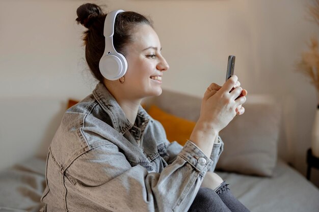 自宅のベッドに座ってスマートフォンで自分撮りをしているカジュアルな服を着た若い美しい女性携帯電話を使ってインターネットでサーフィンをしている女の子が友達とビデオ通話をするインフルエンサー