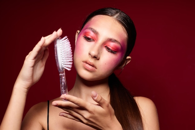 Young beautiful woman with a comb in hand bright makeup posing fashion emotions pink background unaltered