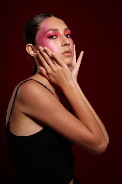 Молодая красивая женщина с творческим макияжем на лице позирует на фоне в студии