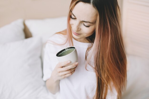 自宅のベッドで一杯のコーヒーと若い美しい女性