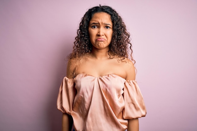 Young beautiful woman with curly hair wearing casual tshirt standing over pink background depressed and worry for distress crying angry and afraid Sad expression