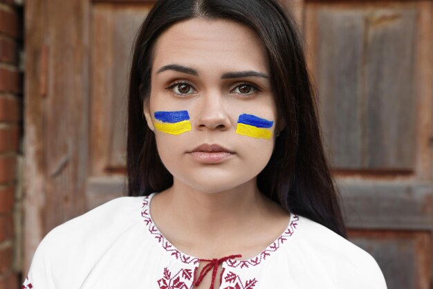 Young beautiful woman with drawings of Ukrainian flag on face near wooden door