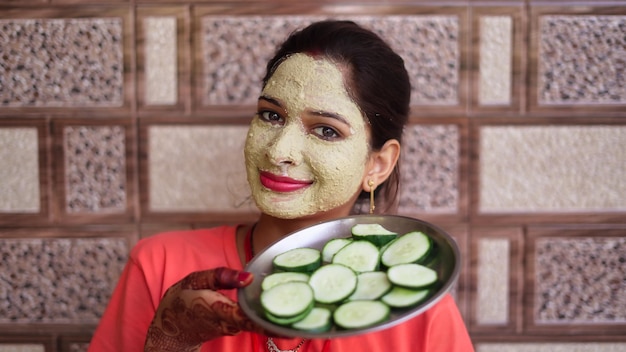 Foto giovane donna bellissima con un pacco per il viso e fette di cetriolo fresco sugli occhi bellezza cura della pelle spa